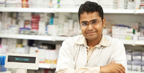 Male pharmacist stood in front of shelves of medication